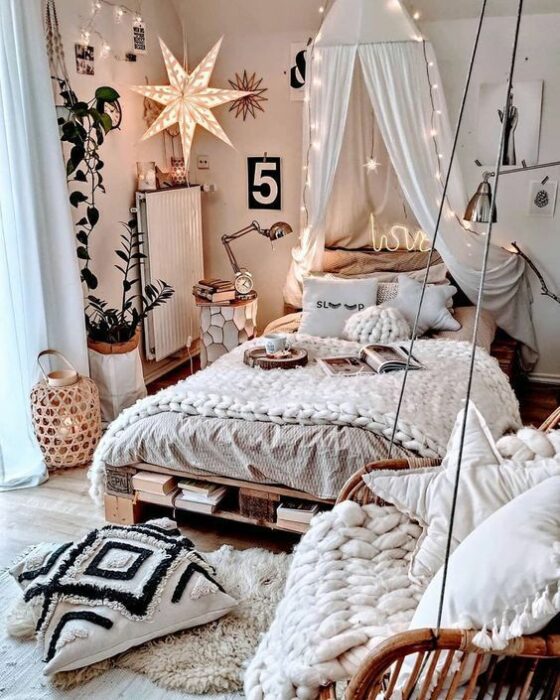 Habitación acogedora con paredes blancas, cama con cobijas blancas tejidas y cojines también blancos, decorada con luces al estilo princesa. En el piso hay una alfombra blanca de peluche