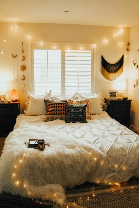 Habitación blanca acogedora con cama de colcha blanca y cojines de cuadros, ubicada junto a la ventana con luces en el techo