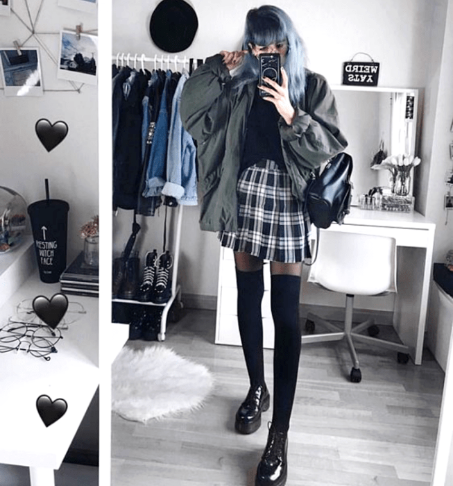 Chica de cabello azul largo con un top negro, chaqueta oversized verde oscuro, minifalda de tablones escocesa, medias negras largas, mochila negra de cuero y mocasines de plataforma