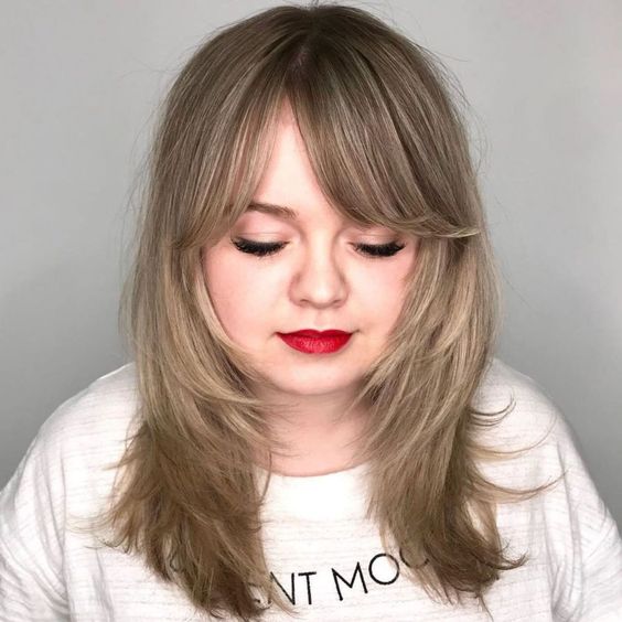 Chica rubia con rostro redondo con melena corta, labial rojo y fleco de lado