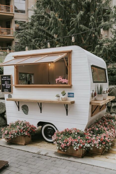Mini camión de comida blanco con detalles cafés rodeado de flores rosas
