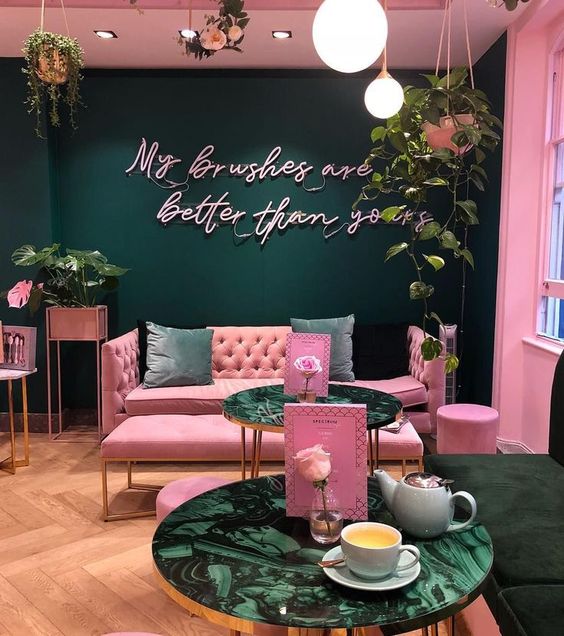 Restaurante con pared verde esmeralda y demás en rosa, piso de madera y sillón rosa con cojines verdes