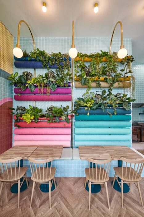 Pared de restaurante azul con macetas de colores y mesas redondas de madera