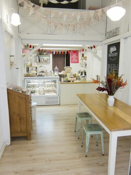 Cafetería blanca con mesa rectangular de madera y bancos de metal menta