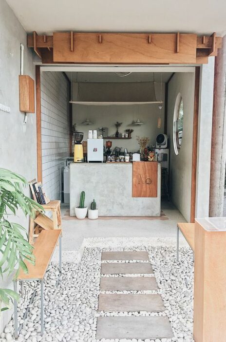 Mini restaurante de concreto con mesas y detalles en madera, decorado con plantas y cactus