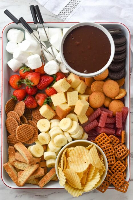 Plato grande con bombones, galletas, plátano y dulces con un recipiente redondo de Nutella