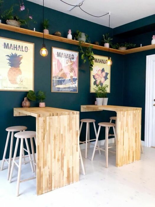 Restaurante con pared verde esmeralda adornada con cuadros tropicales y mesas de madera