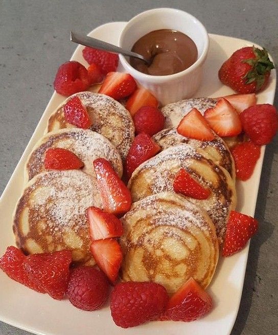 Plato rectangular grande con hotcakes decorados con fresas y un vasito de Nutella