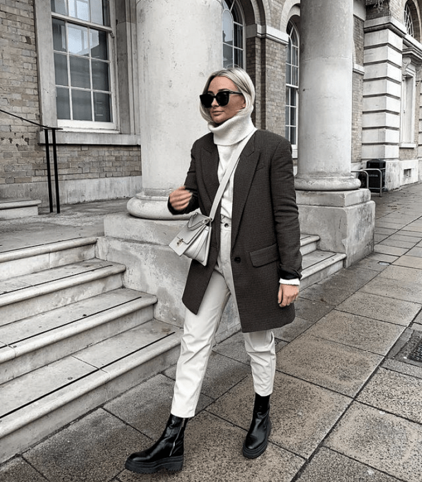 chica rubia platinada usando lentes de sol, suéter blanco de cuello alto, pantalones de mezclilla blanco, botas de cuero negras