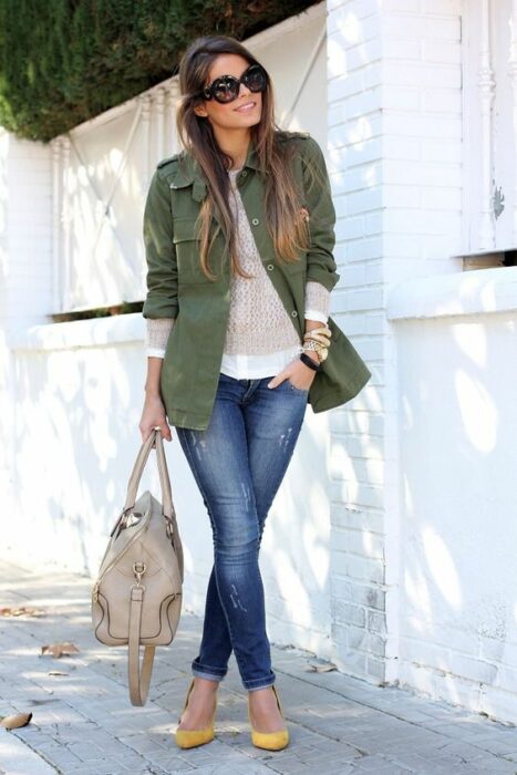 Chica usando tacones, jeans y blusa blanca con blazer color verde army y un bolso de mano beige