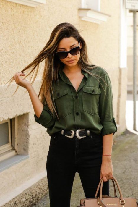 Chica usando jeans negros, cinturón, lentes de sol y camisa verde army