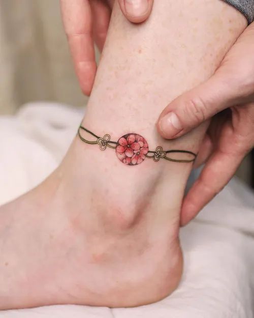 Tatuaje en el tobillo de amuleto asiático color rosa con cadena dorada