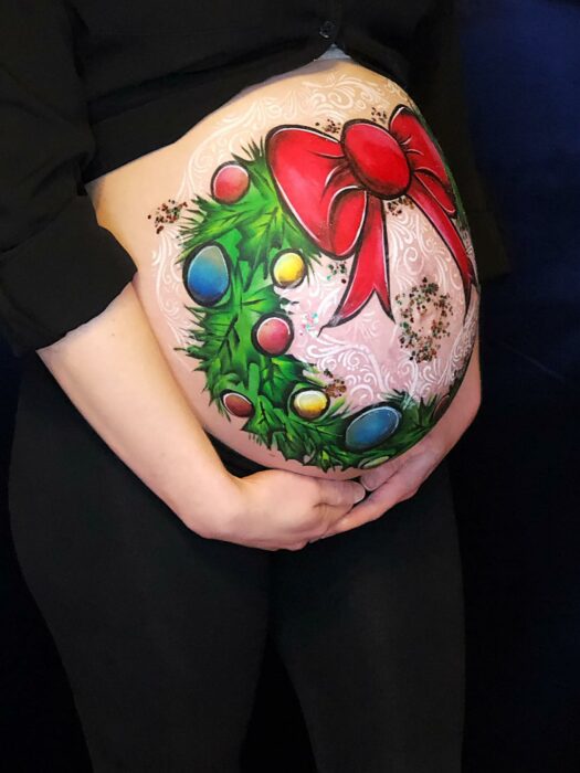 Mujer con la pancita pintada con una corona navideña; Ideas para pintar tu panza de embarazada este diciembre