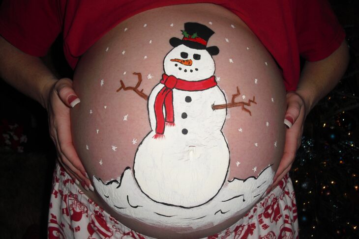 Mujer con la pancita pintada con un muñeco de nieve; Ideas para pintar tu panza de embarazada este diciembre