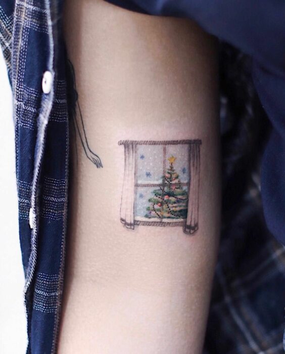 Chica con tatuaje de ventana mostrando un árbol navideño; Tatuajes miniatura para las que aman la Navidad