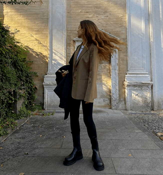 mujer de cabello claro wearing camisa blanca, abrigo beige oscuro, jeans ajustados negros, abrigo negro y botas de suela gruesa negras
