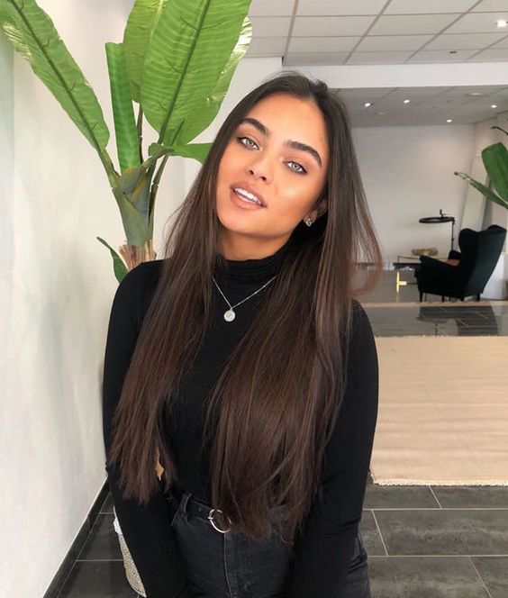 Chica morena de ojos verdes con cabello largo castaño con blusa de manga larga y cuello alto