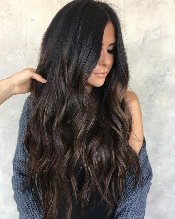Chica morena de cabello largo en capas rizado con suéter gris mirando hacia abajo