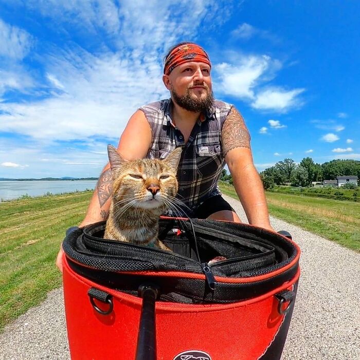 Dean Nicholson y su gata en una bicicleta Nala en el campo con cielo azul, pasto verde