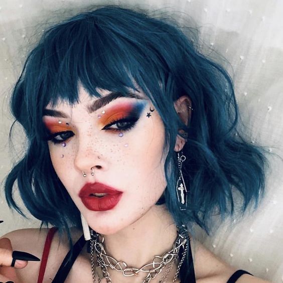 Chica de piel clara con melena corta color azul con labial rojo y ojos con sombra color naranja, azul y negro