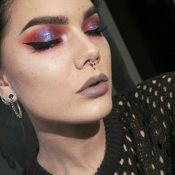 Chica de piel clara con labial gris y ojos con sombras moradas y naranjas con efecto iridiscente