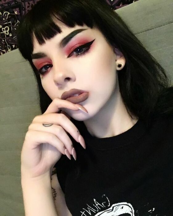 Chica de piel blanca de cabello negro y fleco con labial nude y smokey eye en color rojo con delineado negro intenso