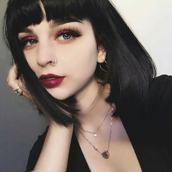 Chica de piel clara con cabello corto negro con fleco y labial rojo y sombras brillantes rojas