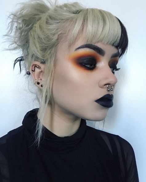 Chica rubia con coleta alta y fleco bicolor con labial negro y smokey eye negro con naranjas