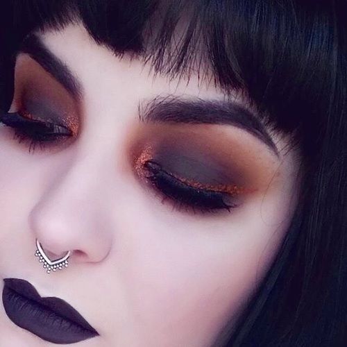 Chica de piel clara con labial morado oscuro con smokey eye negro con naranja y delineado brillante color marrón