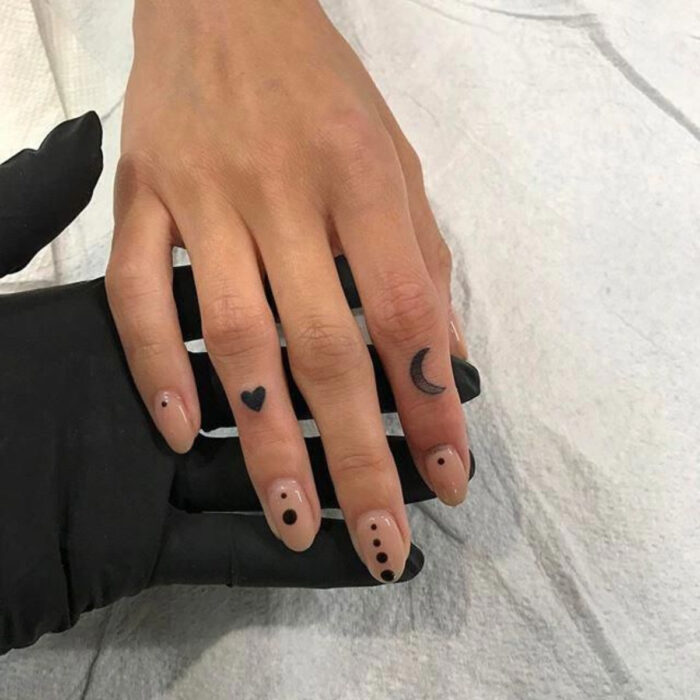 Manos elegantes con manicura, uñas cortas y redondas en nude decoradas con puntos, dedos tatuados con corazón y luna