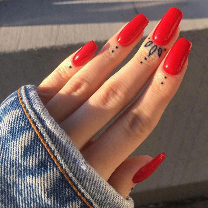 Manos elegantes con manicura, uñas largas cuadradas en rojo, dedos con tatuajes tribales de puntos y flores