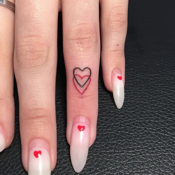 Manos elegantes con manicura, uñas largas stiletto en esmalte blanco mármol con diseño de corazón, dedo con tatuaje de corazones negro y rojo