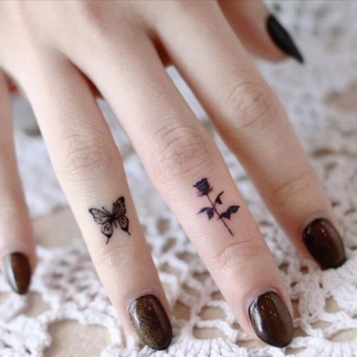 Manos cuidadas con manicura, uñas cortas redondas en café con brillos, dedos tatuados con mariposa y rosa