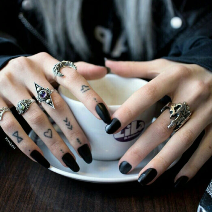 Manos elegantes con manicura, uñas largas y cuadradas, dedos con tatuajes minimalistas de puntos, flechas, corazones, reloj de arena, anillos en lunar, mujer bebiendo café en una taza blanca