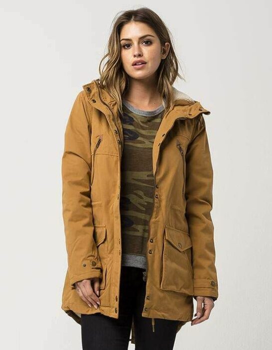 Chica con chamarra cazadora mostaza, suéter y jeans oscuros