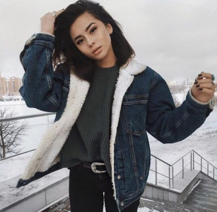 Chica con chaqueta de mezclilla con peluchito, blusa verde oscuro y jeans negros