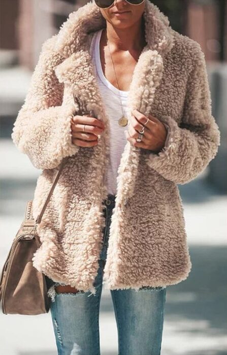 Chica con chaqueta furry color arena, blusa blanca, jeans y bolsa de mano