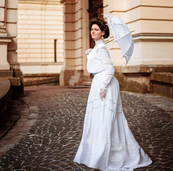 Mila Povoroznyuk usando un vestido de época de manga larga color blanco con una sombrilla del mismo color