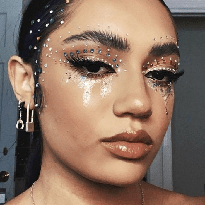 chica morena usando maquillaje con sombras neutrales, glitter plateado, dorado, delineador negro, pestañas postizas y hightliter 