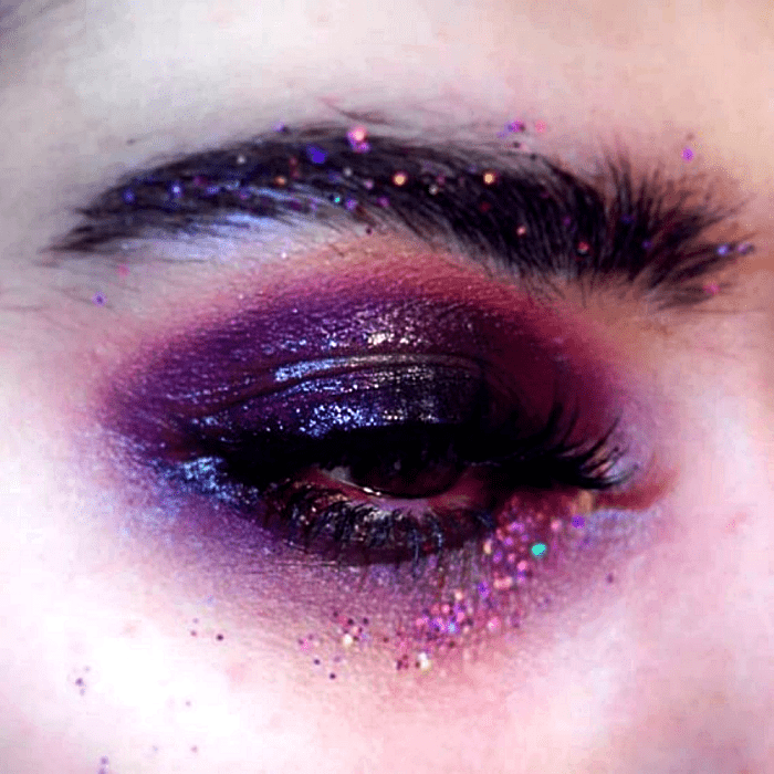 maquillaje morado intenso, con sombras guindas, moradas y rosas, con glitter rosa fucsia y delineado negro