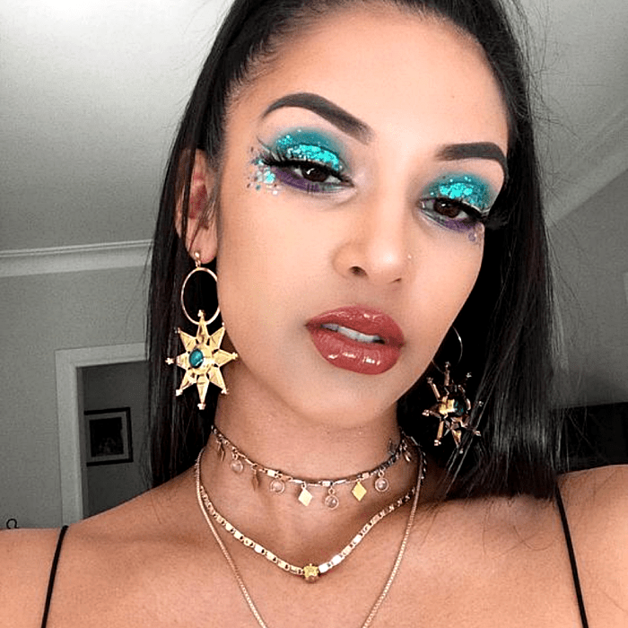chica morena usando maquillaje de sombras azules, turquesa, delineado negro, glitter plateado y azul claro