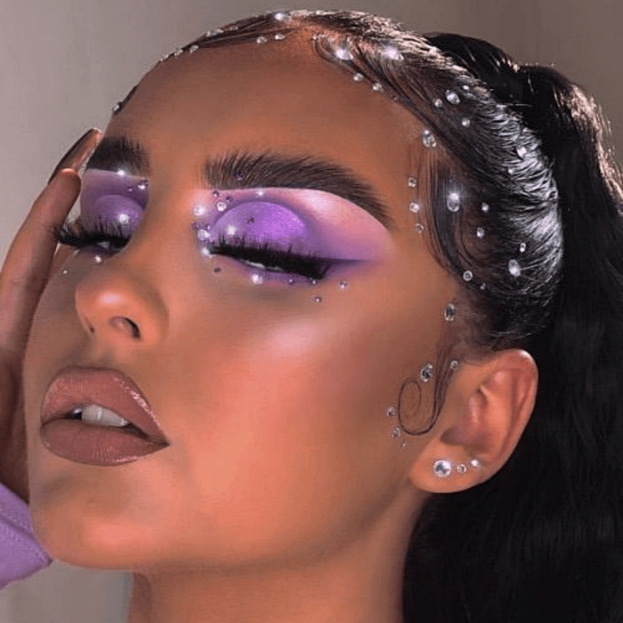 chica morena usando sombras moradas, lilas y rosas pastel, con glitter rosa y plateado y delineado negro
