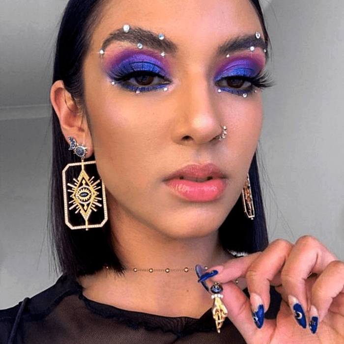 chica morena con maquillaje morado, rosa y azul, con glitter en las cejas y delineado negro
