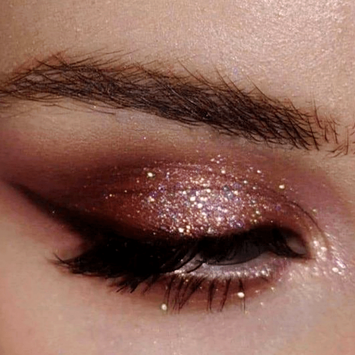 maquillaje rosa intenso con sombras café, beige, rosa y delineado negro, glitter multicolor
