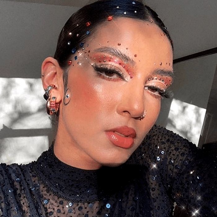 chica morena con maquillaje de sombras rosas, delineado gráfico, glitter de colores, blush naranja y lipstick naranja