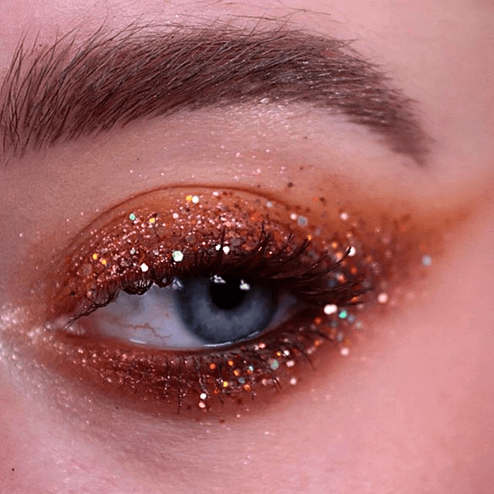 maquillaje con sombras cafés, doradas y naranjas, con glitter de colores