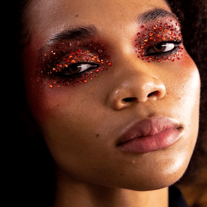 chica morena con maquillaje rosa, fucsia, café y naranja con sombras intensas y delineado gráfico y glitter