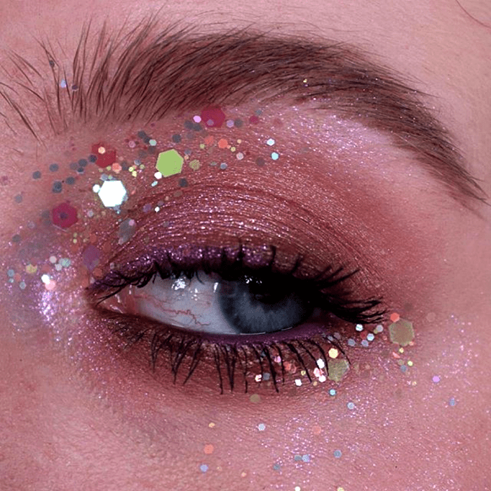 maquillaje con sombras neutrales, delineado negro y glitter multicolor
