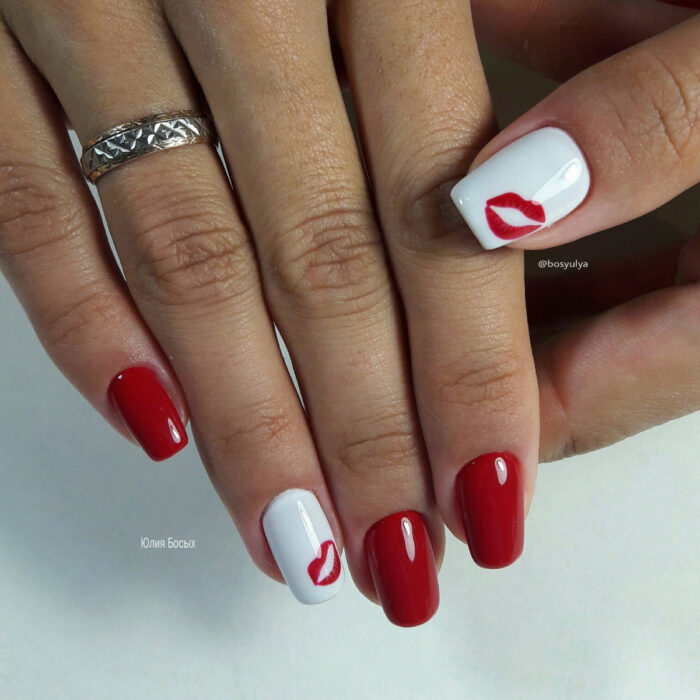 Manos con uñas largas cuadradas pintadas con esmalte rojo y blanco, con diseño de besos plantados