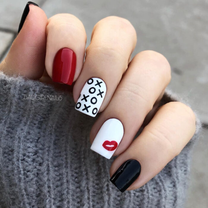 Manos con uñas largas y cuadradas pintadas en esmalte rojo, negro y blanco, con diseño de beso plantado y xoxo